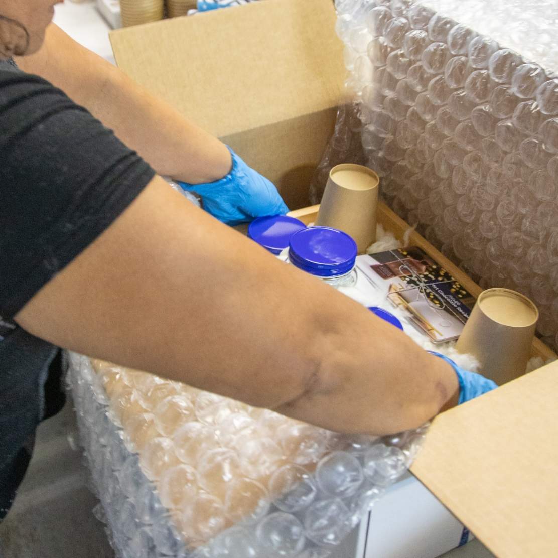 Fulfillment team member placing fully loaded fairlife hot chocolate kit into a bubble wrapped lined mailing box