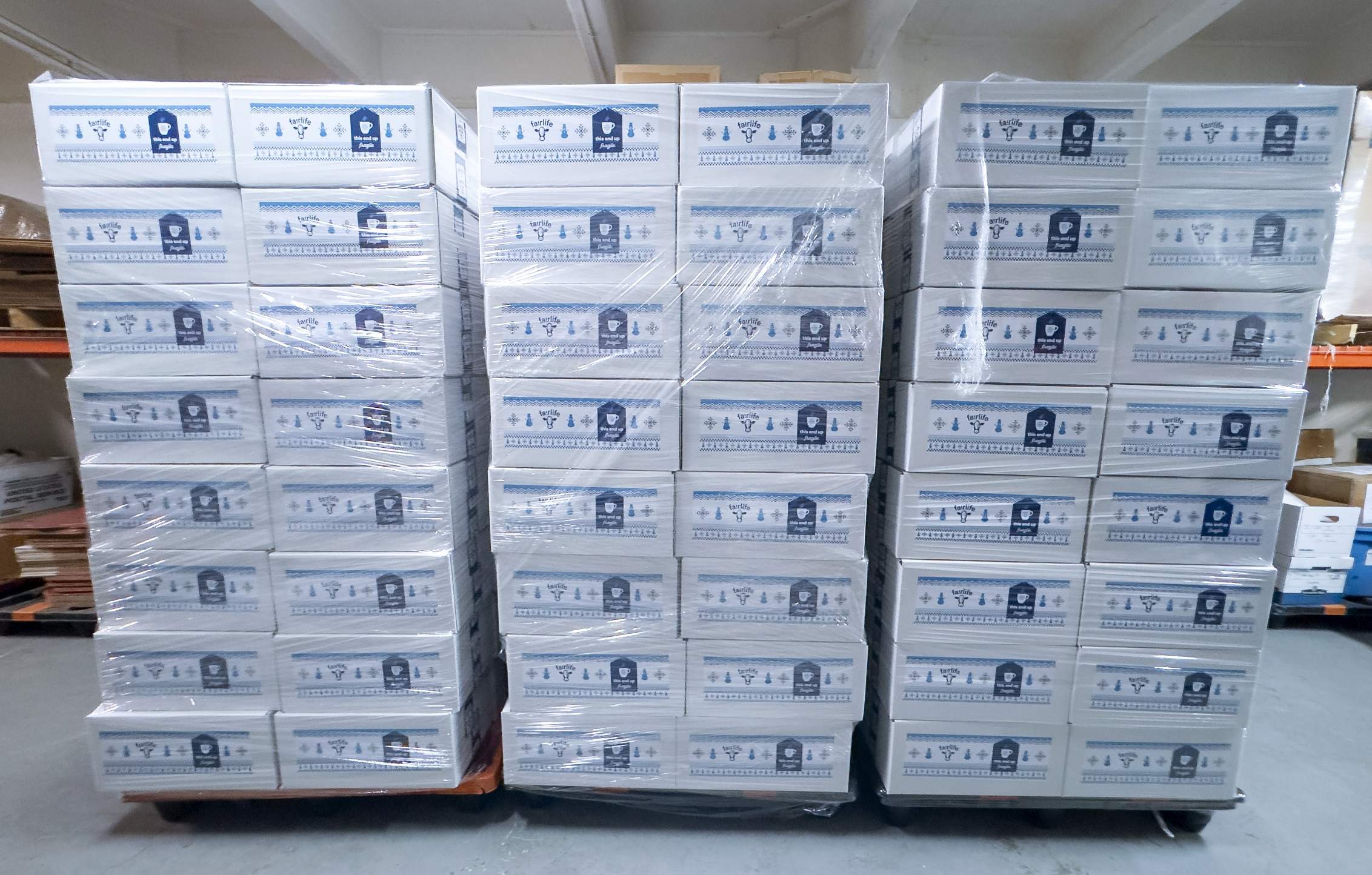 Straight on shot of three rows of plastic wrapped pallets of stacked and sealed mailing boxes in a warehouse