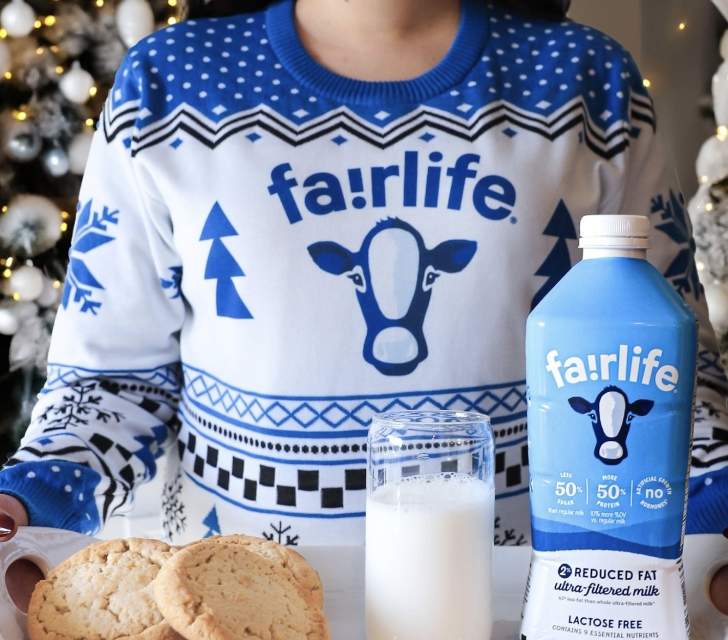 woman wearing a fairlife holiday sweater and she's carrying a tray with milk and cookies